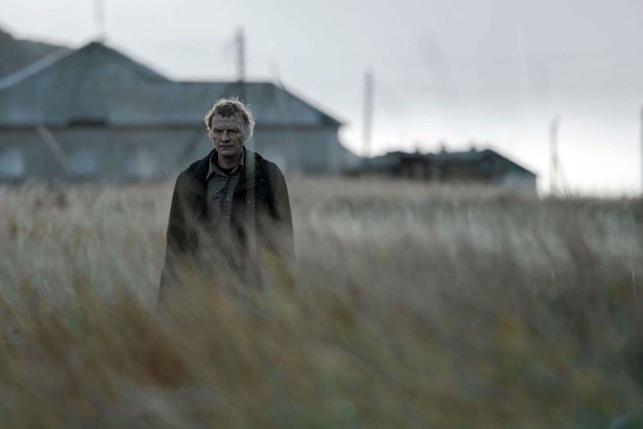 Still from feature film Leviathan, featuring a pensive man in his fifties, stoically walking through an overgrown field in a rural setting.